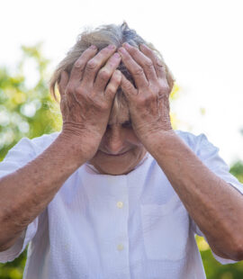 A victim o​​f elder abuse in a white shirt with her face in her hands who is wondering, Is elder abuse a felony in California?