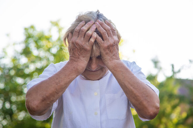 A victim o​​f elder abuse in a white shirt with her face in her hands who is wondering, Is elder abuse a felony in California?