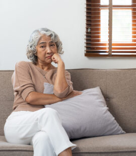 A distressed senior woman contemplating the consequences of the financial crimes against the elderly she’s experienced; understanding what the two categories of elderly financial abuse crimes are is the only way to prevent this scenario from playing out.