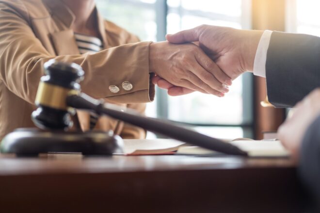 A corporate trust attorney shaking hands with a client with a gavel in the forefront of the picture.