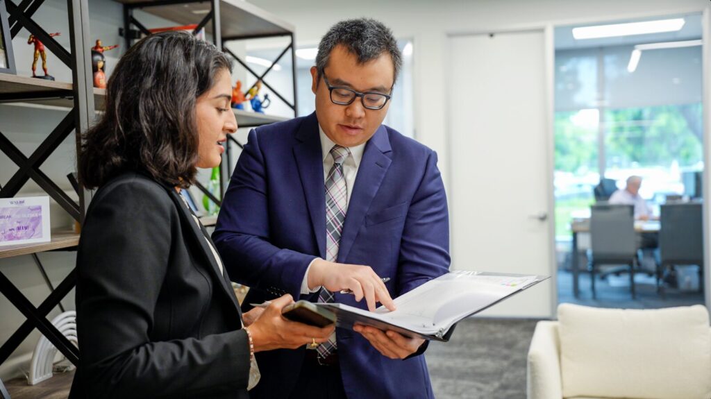 Andrew and Anum standing in the Gokal Law Group office and referring to documents as they discuss the grounds for disinheritance in California.